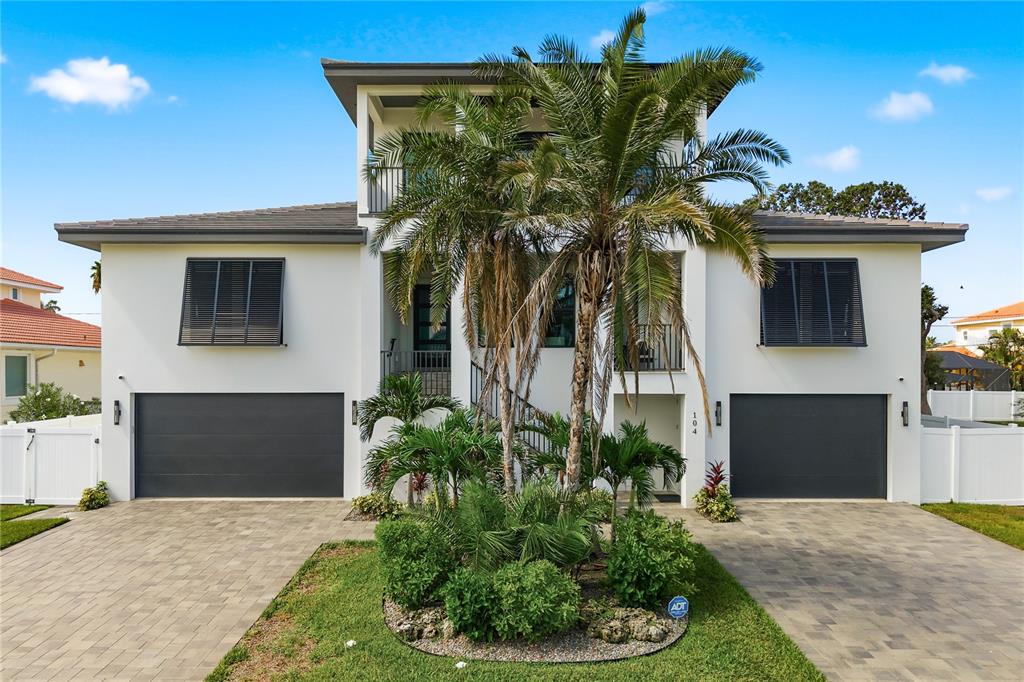 A three-story white house with two garages, a central palm tree, and a paved driveway — 104 17TH STREET, BELLEAIR BEACH, FL