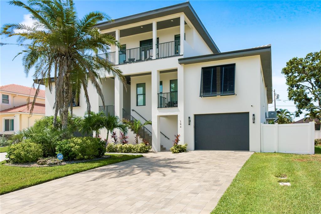 A modern two-story house features a paved driveway, a garage, and a second-floor balcony — 104 17TH STREET, BELLEAIR BEACH, FL