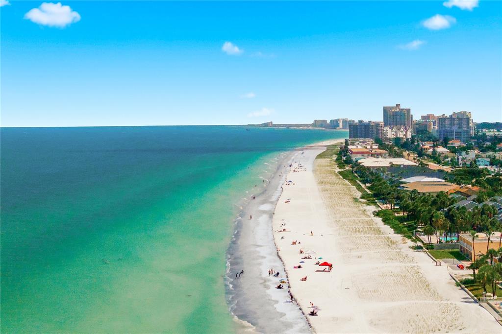 An aerial view of a sandy beach with turquoise water and coastal buildings in the distance — 104 17TH STREET, BELLEAIR BEACH, FL