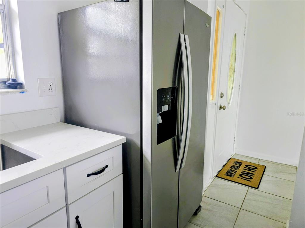 A stainless steel side-by-side refrigerator stands next to white cabinets and a door — 4008 BIANCA STREET, SEBRING, FL