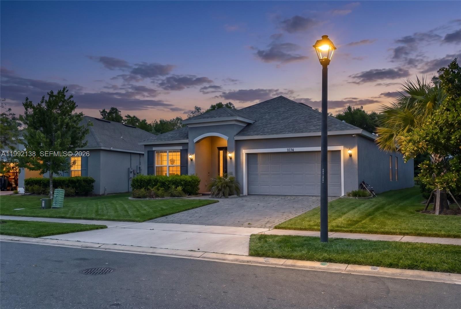 A single-story gray house with a paved driveway and a street lamp in the foreground — 1034 CHELAN FALLS DR, Deland FL 32724, DELAND, FL