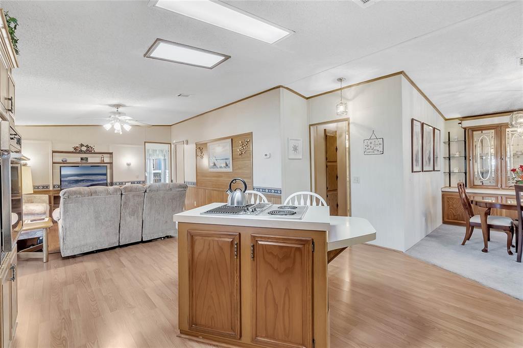 An open-concept kitchen with a center island and wood flooring overlooks a living room — 1690 NASSAU CIRCLE, TAVARES, FL
