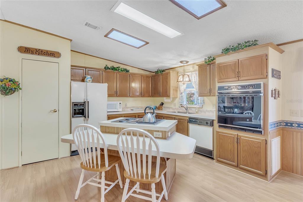 A kitchen features wood cabinets, a central island with seating, and white appliances — 1690 NASSAU CIRCLE, TAVARES, FL