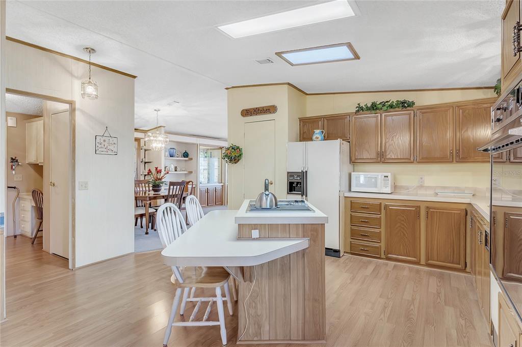 A kitchen with wood cabinets, a center island, and light wood-look flooring — 1690 NASSAU CIRCLE, TAVARES, FL