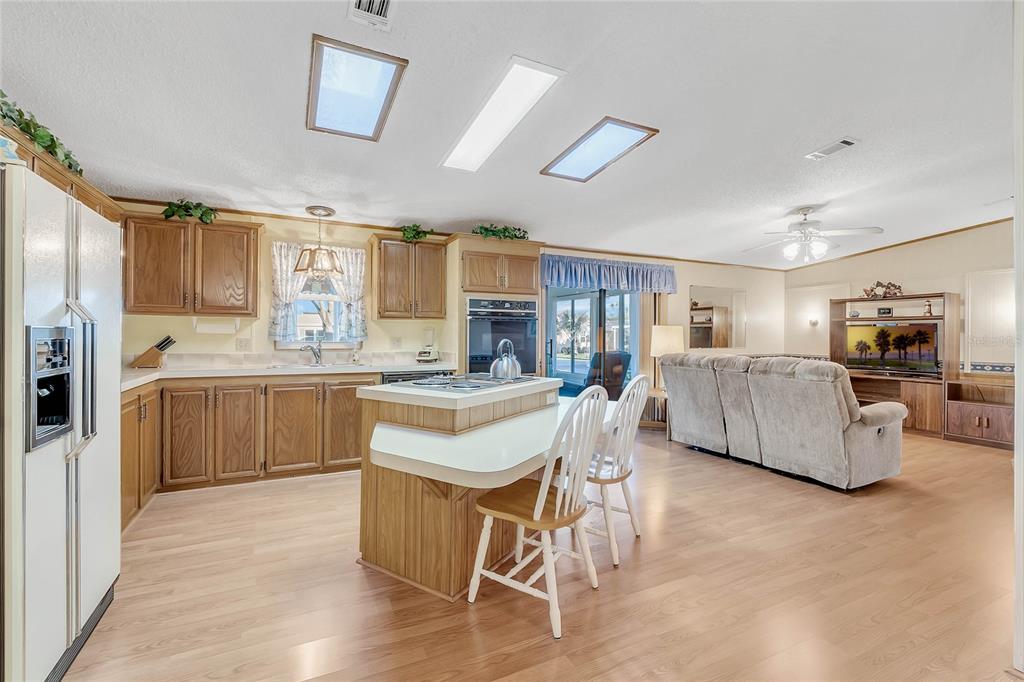 A kitchen with wood cabinets and a center island opens into a living room area — 1690 NASSAU CIRCLE, TAVARES, FL
