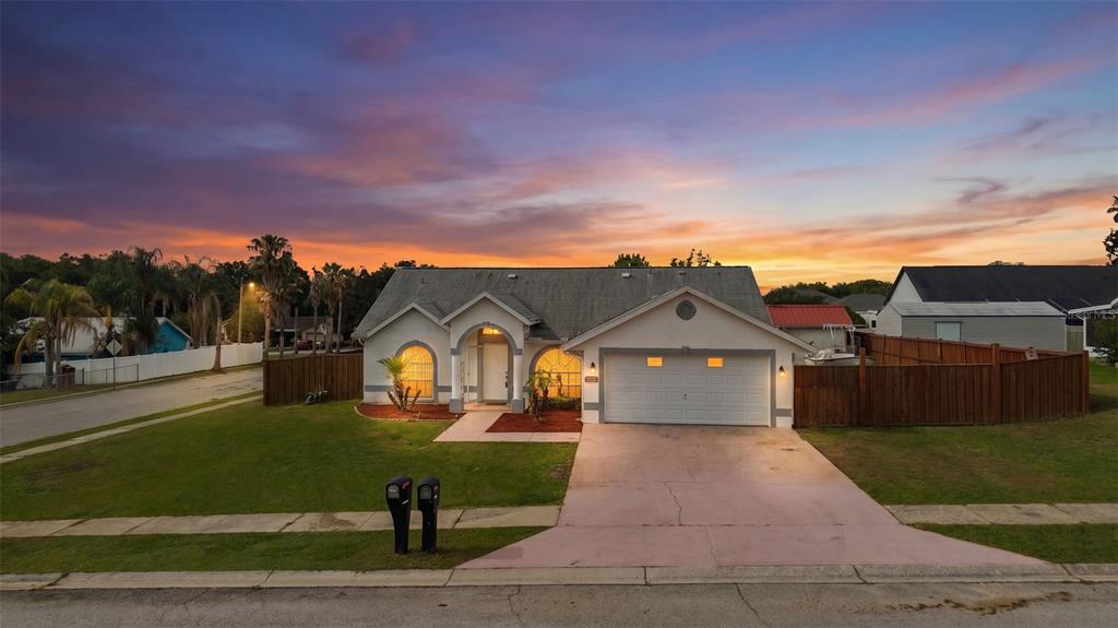 A single-story house with a two-car garage and a wooden fence at sunset — 38912 CARR DRIVE, ZEPHYRHILLS, FL