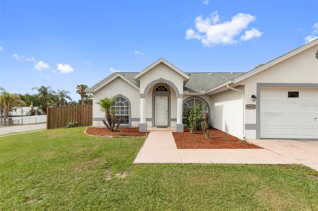 A single-story house with a white stucco exterior, arched entryway, and an attached garage — 38912 CARR DRIVE, ZEPHYRHILLS, FL
