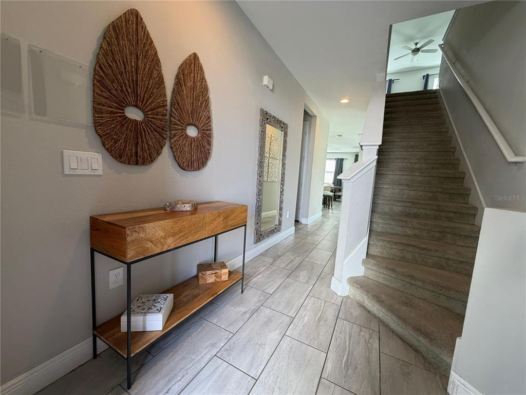 A foyer features a wooden console table, wall art, a mirror, and a carpeted staircase — 7676 FAIRFAX DRIVE, KISSIMMEE, FL