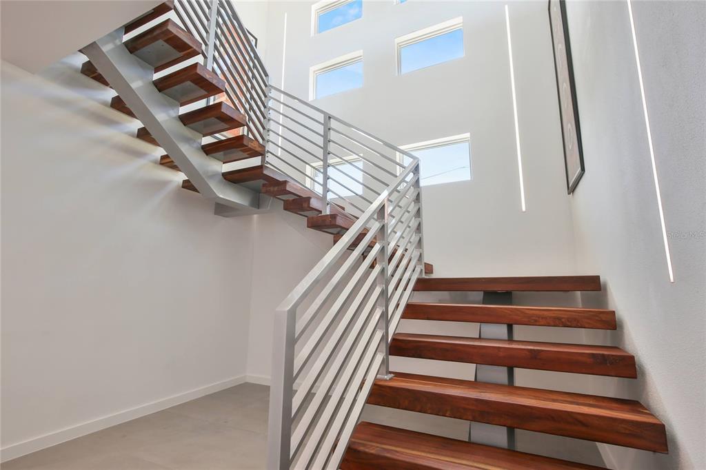 A modern staircase with wooden treads and metal railings in a bright, high-ceilinged entryway — 3939 HIGEL AVENUE, SARASOTA, FL