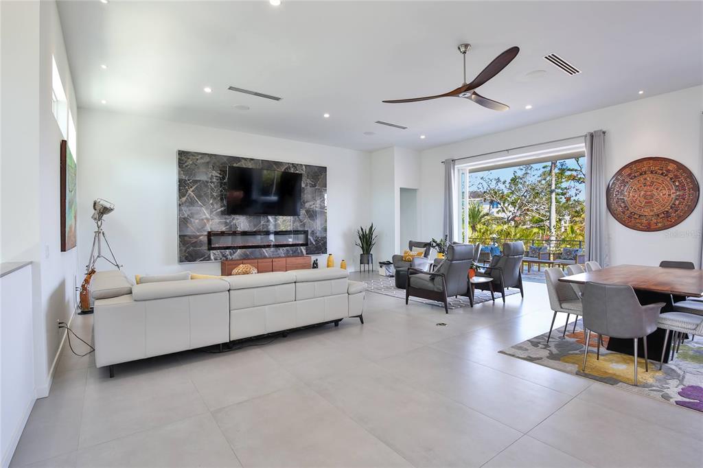 A modern open-concept living and dining area features a marble fireplace wall and large sliding doors — 3939 HIGEL AVENUE, SARASOTA, FL