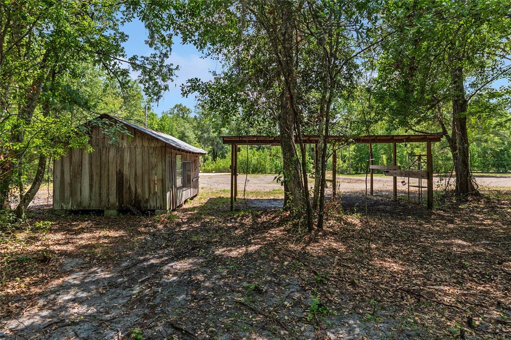 A wooden shed stands next to an open-sided pole barn in a wooded area — 4814 NW 244 AVENUE, ALACHUA, FL