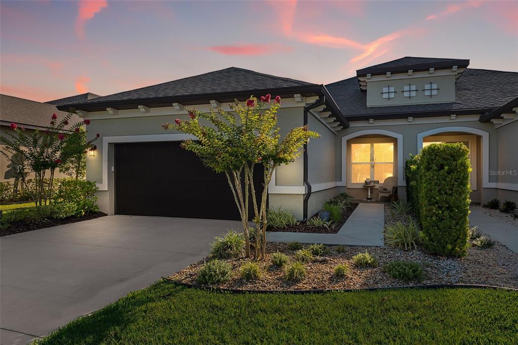 A single-story house exterior features a dark garage door, a landscaped yard, and sunset lighting — 3266 BAILEY ANN DRIVE, ORMOND BEACH, FL