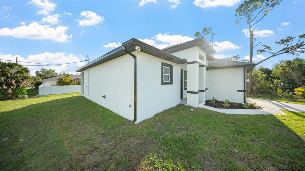 A side view of a white stucco house with dark trim and a grassy yard — 18265 LAKE WORTH BOULEVARD, PORT CHARLOTTE, FL