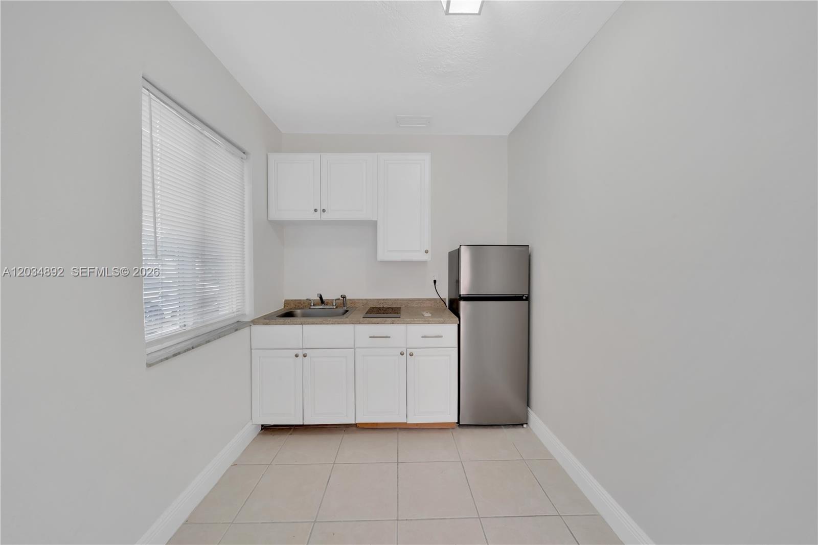 This small kitchen features white cabinets, a stainless steel refrigerator, and light tile flooring — 7555 SW 28th St Rd # b, Miami FL 33155, MIAMI, FL