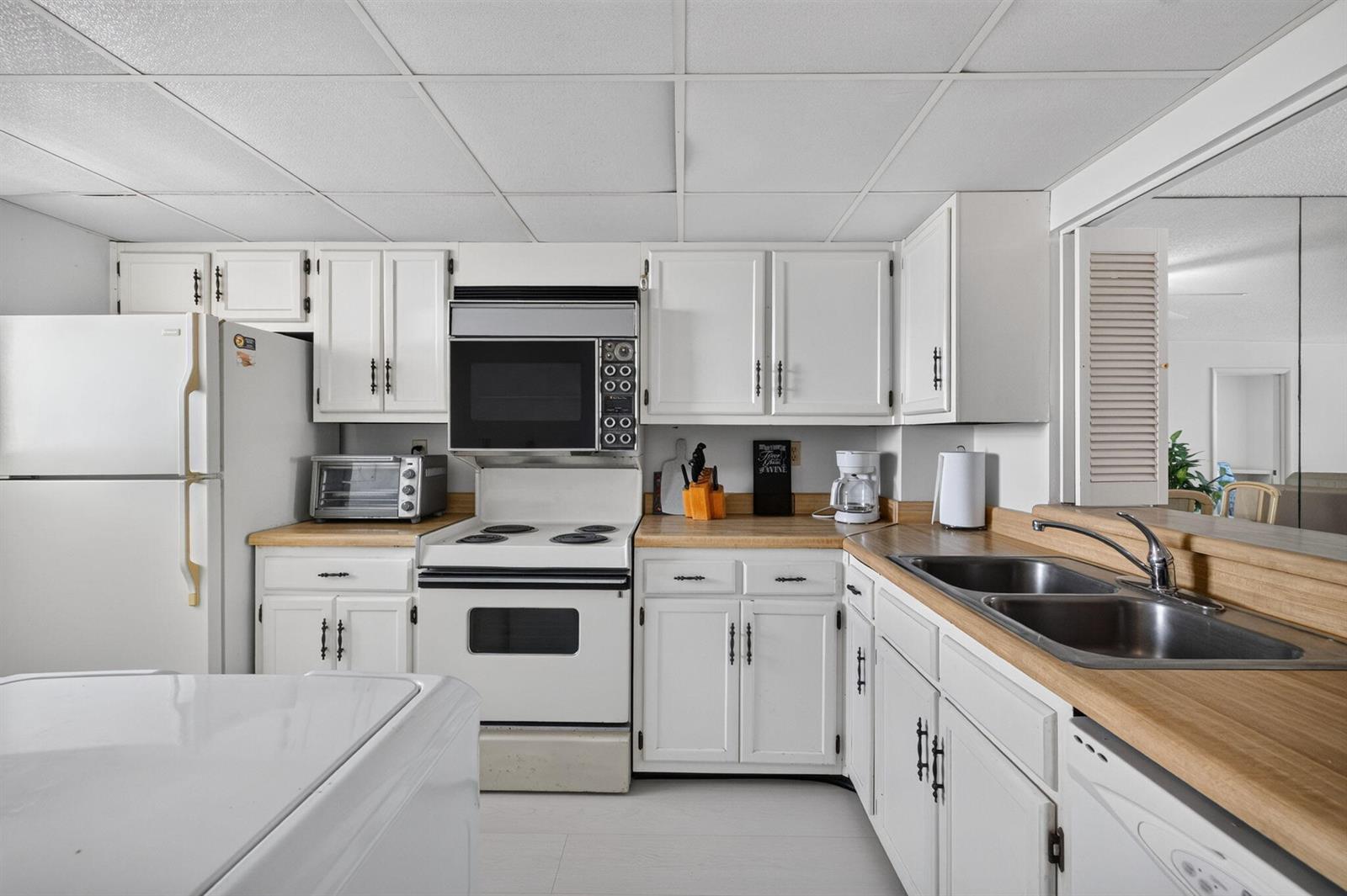 A kitchen features white cabinets, a white stove, a double sink, and light wood countertops — 9900 S Ocean Drive # 1505, Jensen Beach FL 34957, JENSEN BEACH, FL