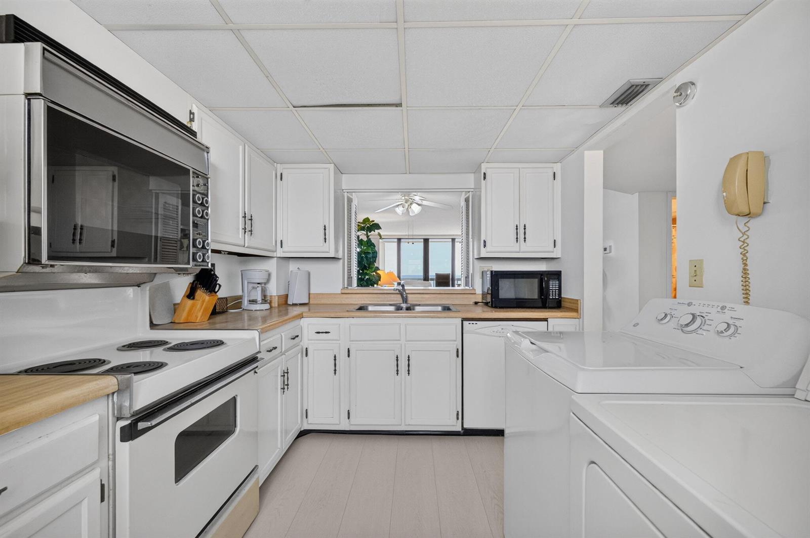 A white kitchen features wood countertops, a pass-through window, and an adjacent laundry area — 9900 S Ocean Drive # 1505, Jensen Beach FL 34957, JENSEN BEACH, FL