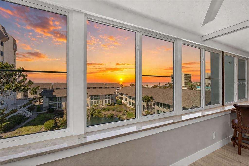 A sunroom with large windows overlooking a sunset, a pond, and neighboring residential buildings — 1080 W PEPPERTREE LANE UNIT 305A, SARASOTA, FL