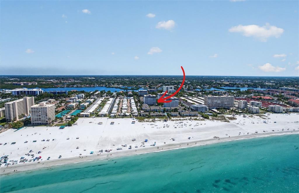 An aerial view shows a beachfront resort complex with a red arrow pointing to a building — 1080 W PEPPERTREE LANE UNIT 305A, SARASOTA, FL