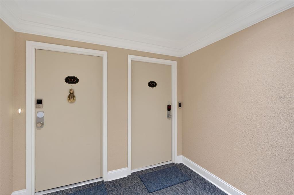 Two apartment doors numbered 303 and 305 are set in a beige hallway with carpet — 1080 W PEPPERTREE LANE UNIT 305A, SARASOTA, FL