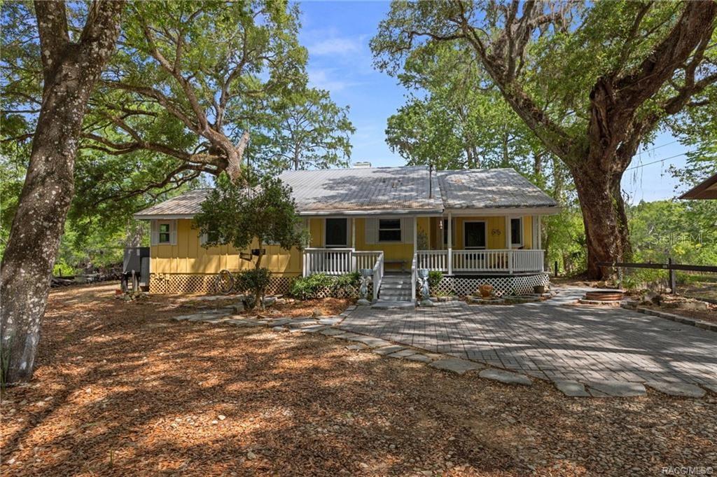A yellow house with a metal roof and a front porch sits among large trees — 3503 E WESTCOVE COURT, DUNNELLON, FL