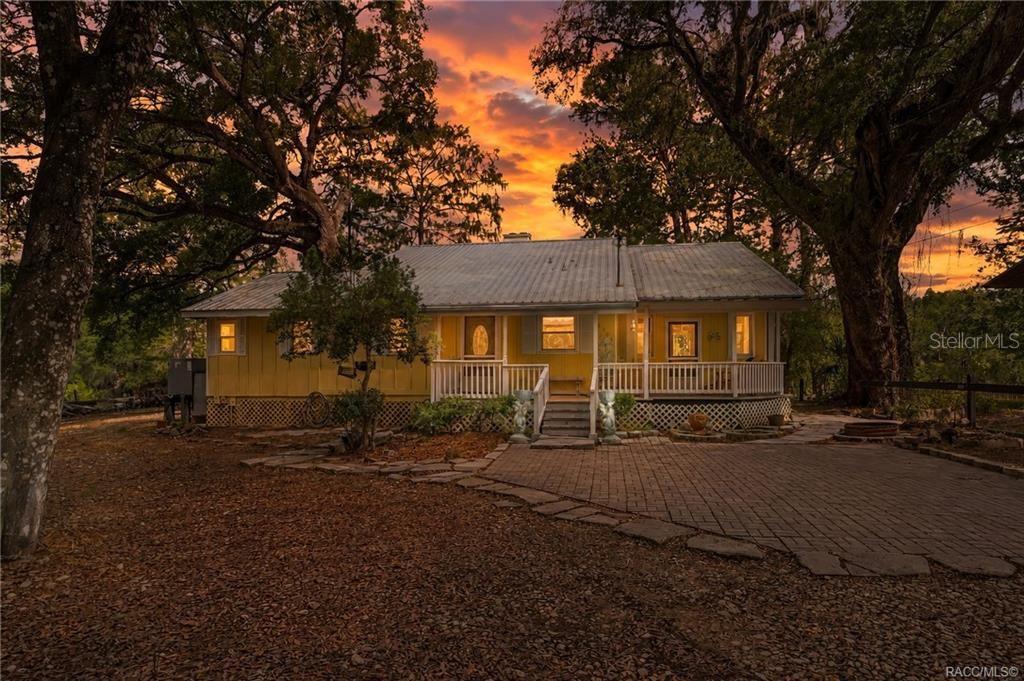 A yellow house with a metal roof and a front porch sits under sunset skies — 3503 E WESTCOVE COURT, DUNNELLON, FL