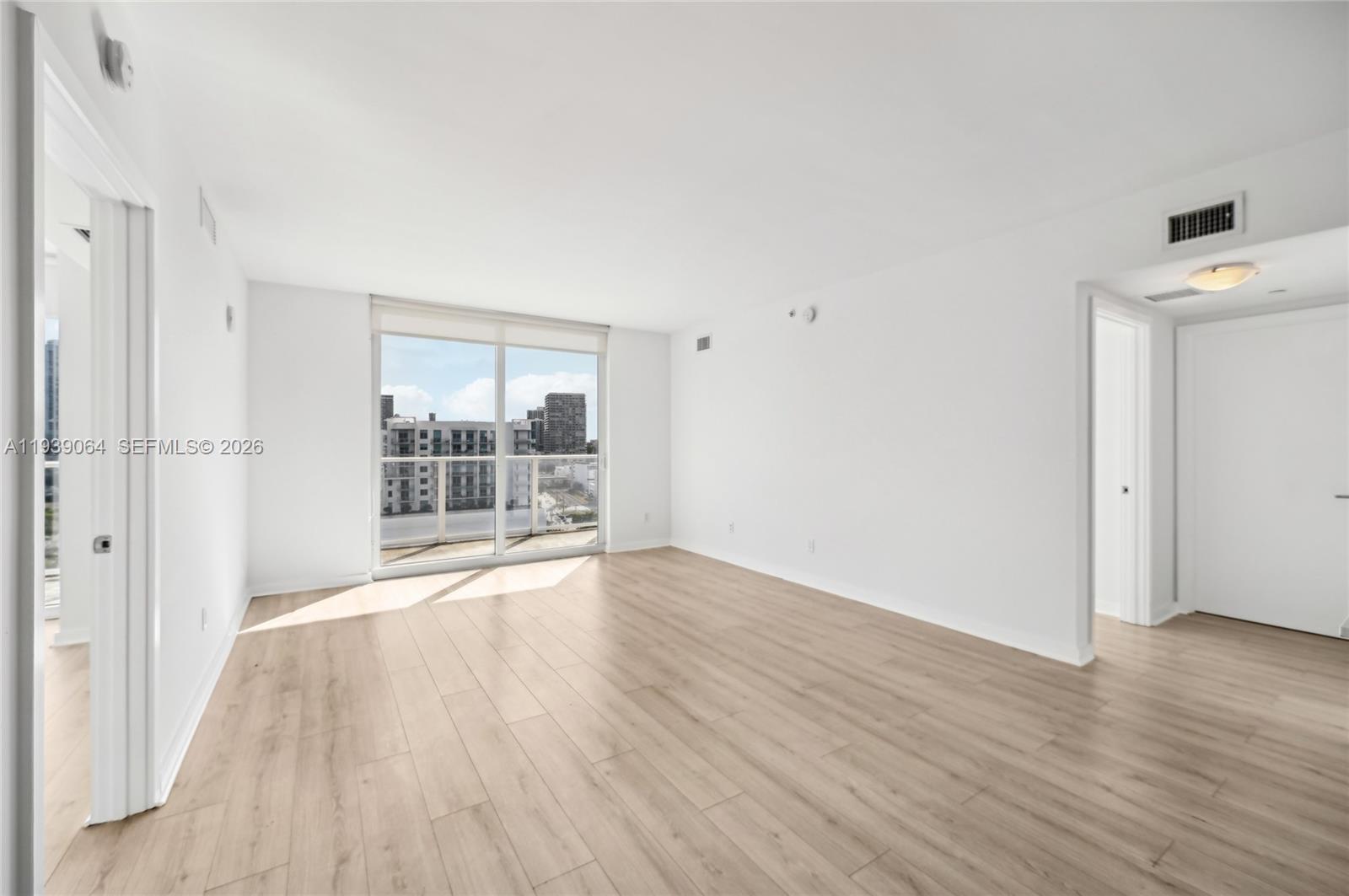 An empty room features light wood-look flooring, white walls, and a sliding glass balcony door — 4250 Biscayne Blvd # 1516, Miami FL 33137, MIAMI, FL
