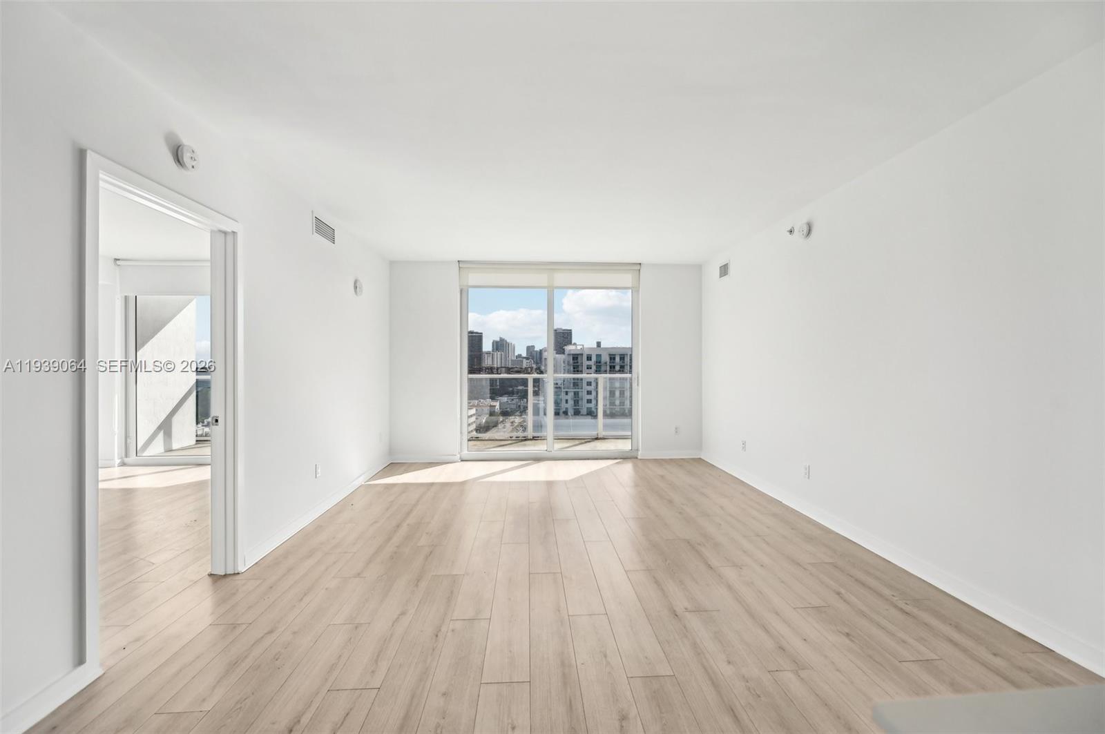 An empty living room features light wood-look flooring, white walls, and a balcony with city views — 4250 Biscayne Blvd # 1516, Miami FL 33137, MIAMI, FL