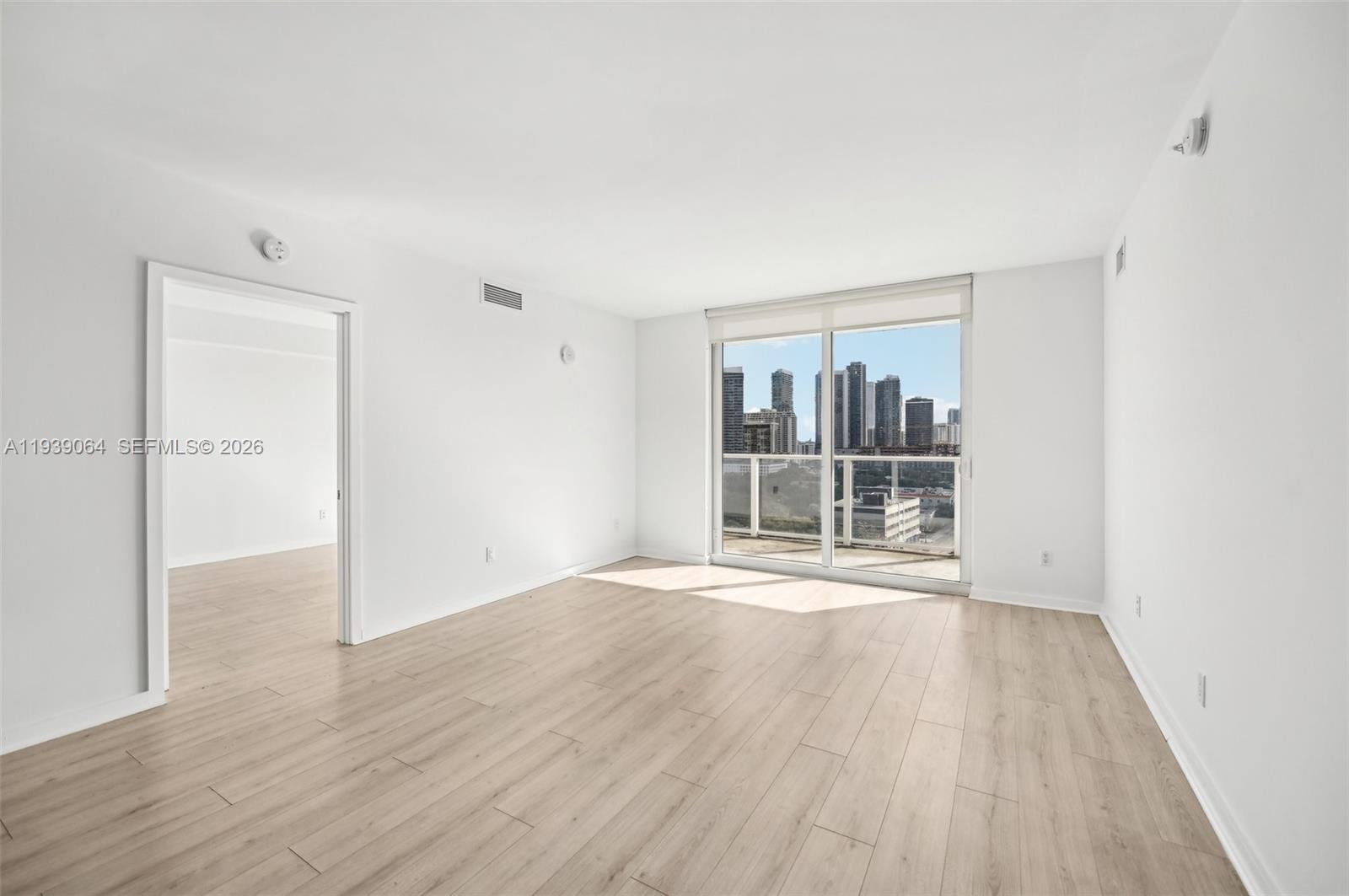 An empty room with light wood-look flooring, white walls, and a balcony overlooking a city — 4250 Biscayne Blvd # 1516, Miami FL 33137, MIAMI, FL