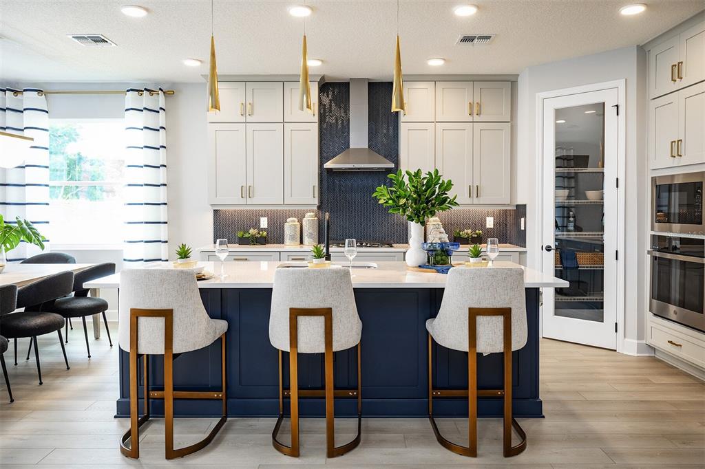 A modern kitchen features a navy blue island, light gray cabinets, and gold pendant lighting — 842 CREEPING FIG STREET, APOPKA, FL