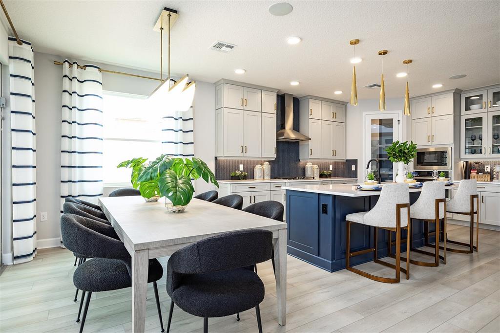 A dining area with a light wood table and dark chairs sits beside a blue-island kitchen — 842 CREEPING FIG STREET, APOPKA, FL