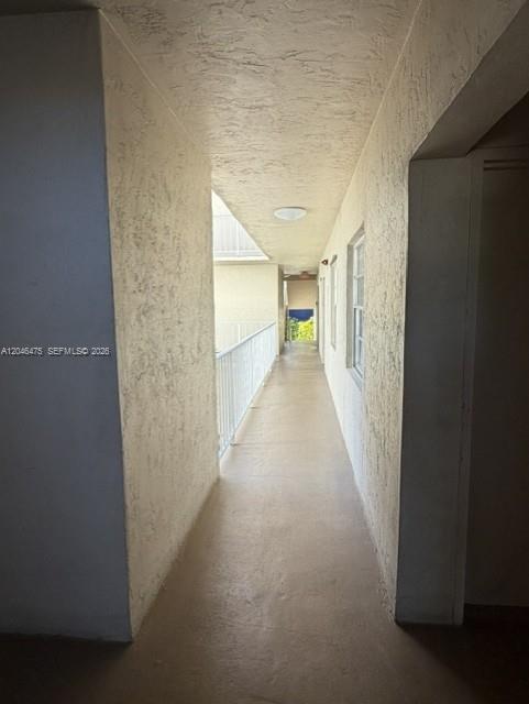 An outdoor apartment building walkway with textured walls, a white railing, and a ceiling light — 7715 SW 86th St # 205, Miami FL 33143, MIAMI, FL