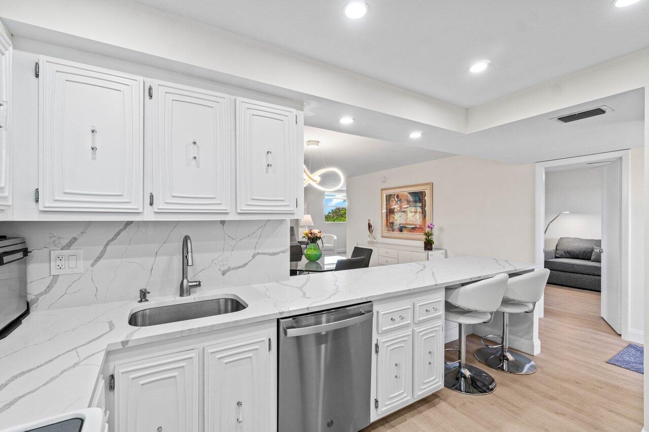 A white kitchen with marble countertops, stainless steel appliances, and a breakfast bar — 6461 NW 2nd Avenue # 411, Boca Raton FL 33487, BOCA RATON, FL