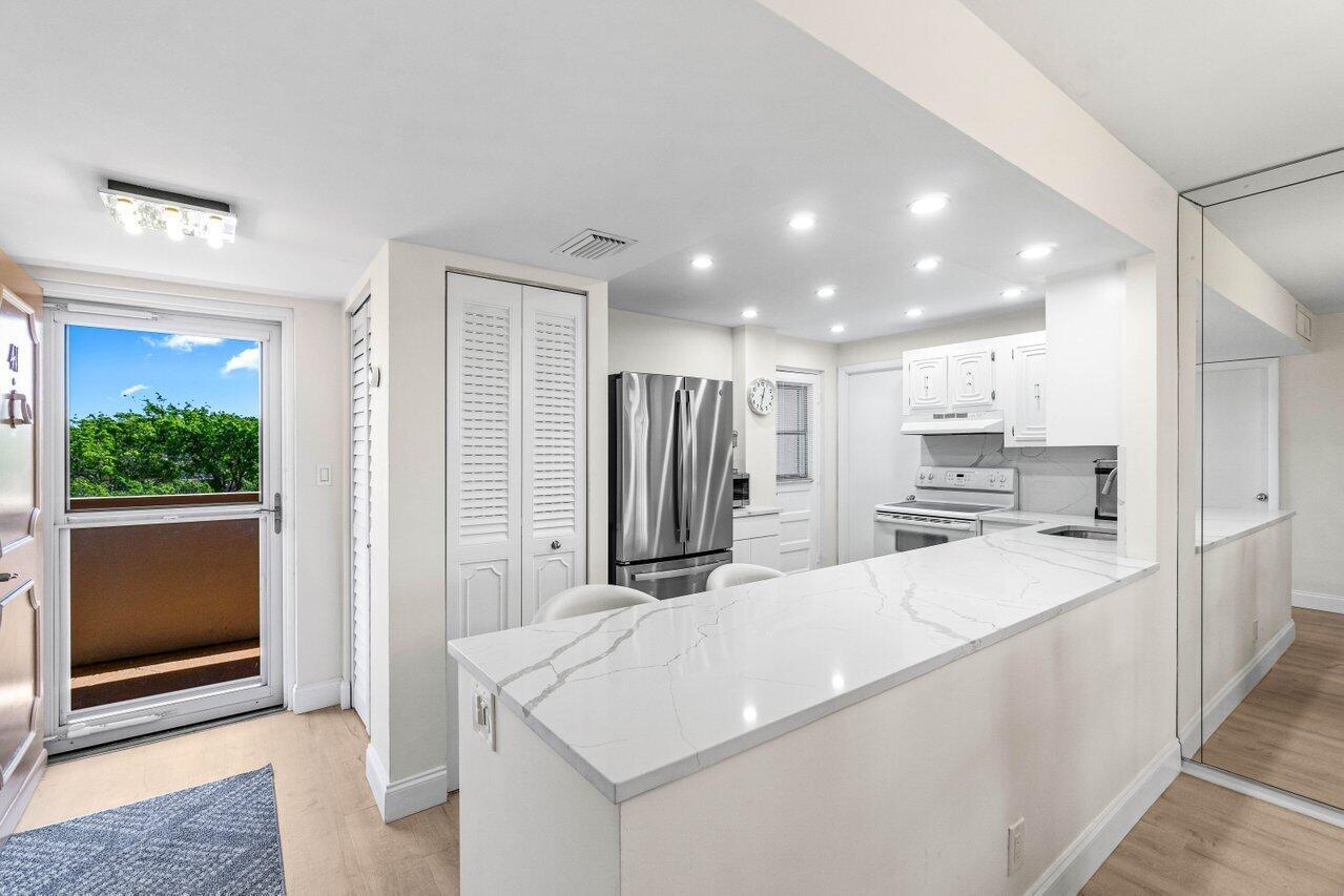 A kitchen features white cabinetry, a marble-topped breakfast bar, and a glass door to outside — 6461 NW 2nd Avenue # 411, Boca Raton FL 33487, BOCA RATON, FL