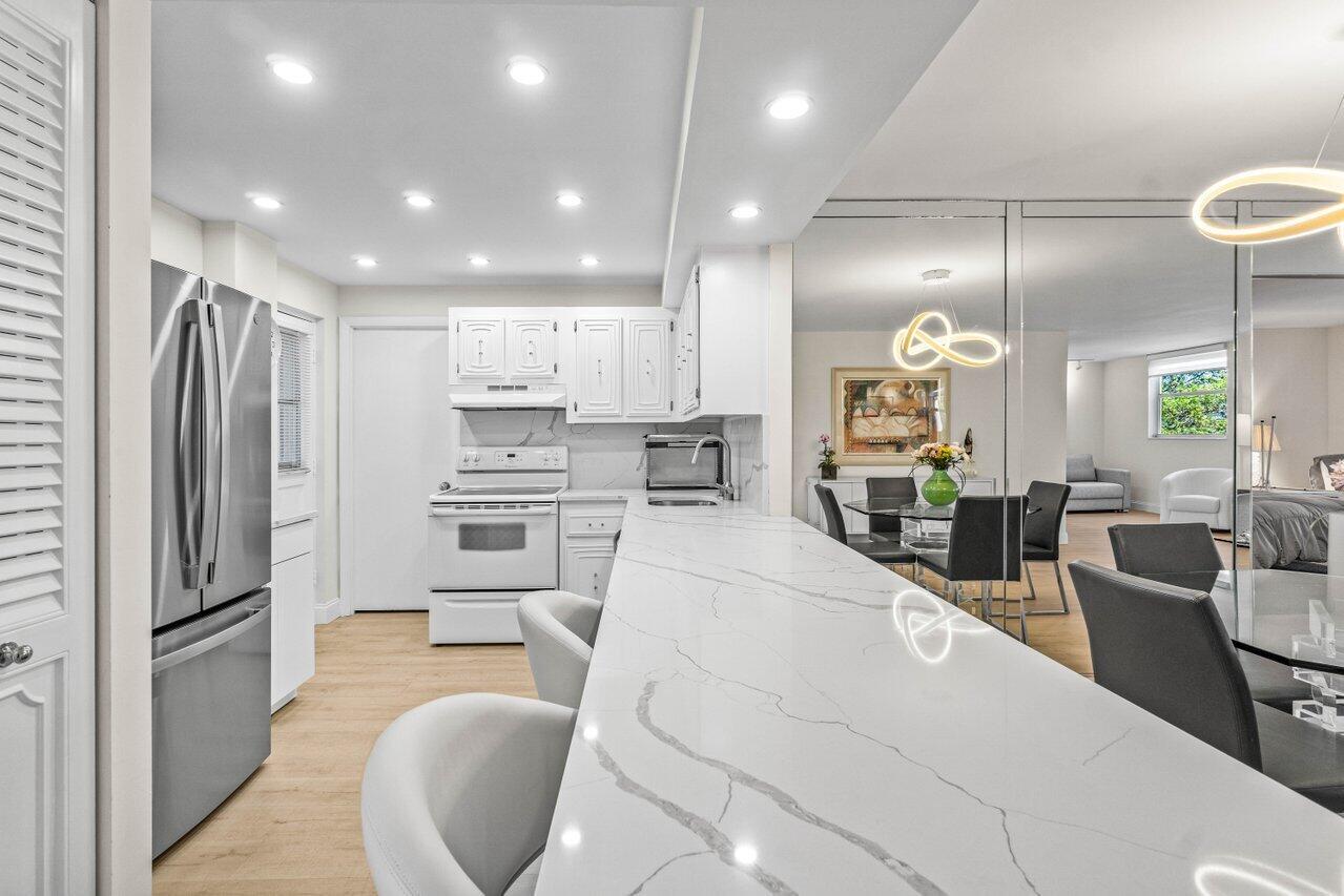 A white kitchen with a quartz breakfast bar overlooks a dining area with mirrored walls — 6461 NW 2nd Avenue # 411, Boca Raton FL 33487, BOCA RATON, FL