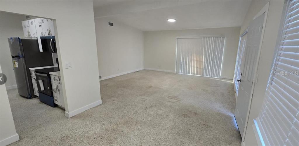 An open-concept living area features beige carpeting, white walls, and an adjacent kitchen with appliances — 1634 BANYAN DRIVE, VENICE, FL