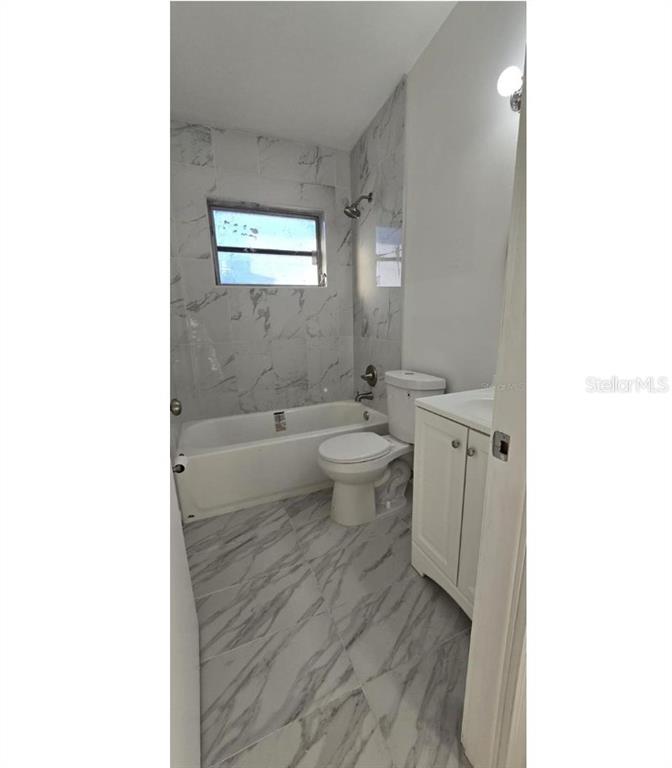 A bathroom features marble-look tile flooring and walls, a bathtub, a toilet, and a vanity — 1634 BANYAN DRIVE, VENICE, FL