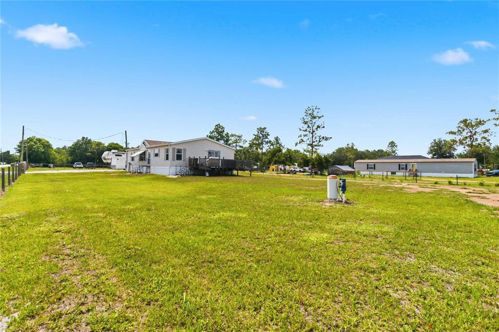 A wide, grassy lot features a light-colored mobile home with a wooden deck — 9109 ATLAS DRIVE, ST CLOUD, FL