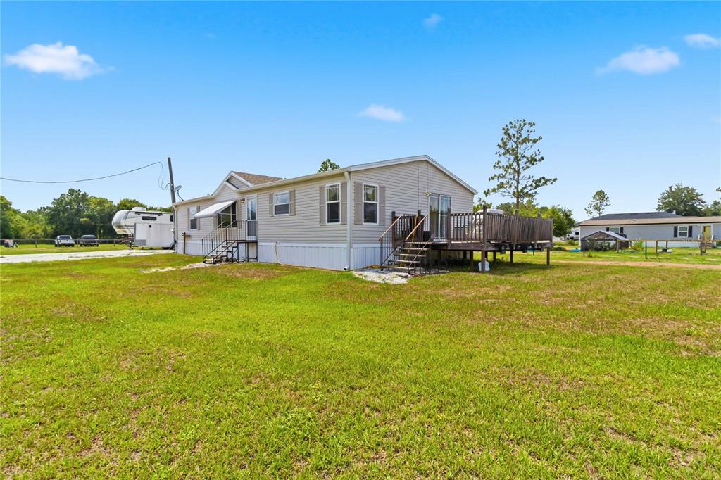 A light-colored manufactured home sits on a grassy lot with a wooden deck — 9109 ATLAS DRIVE, ST CLOUD, FL