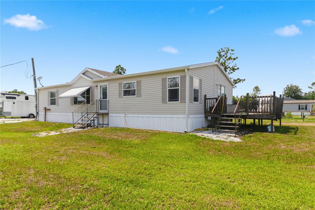 A light-colored manufactured home features a wooden deck and a small set of stairs — 9109 ATLAS DRIVE, ST CLOUD, FL