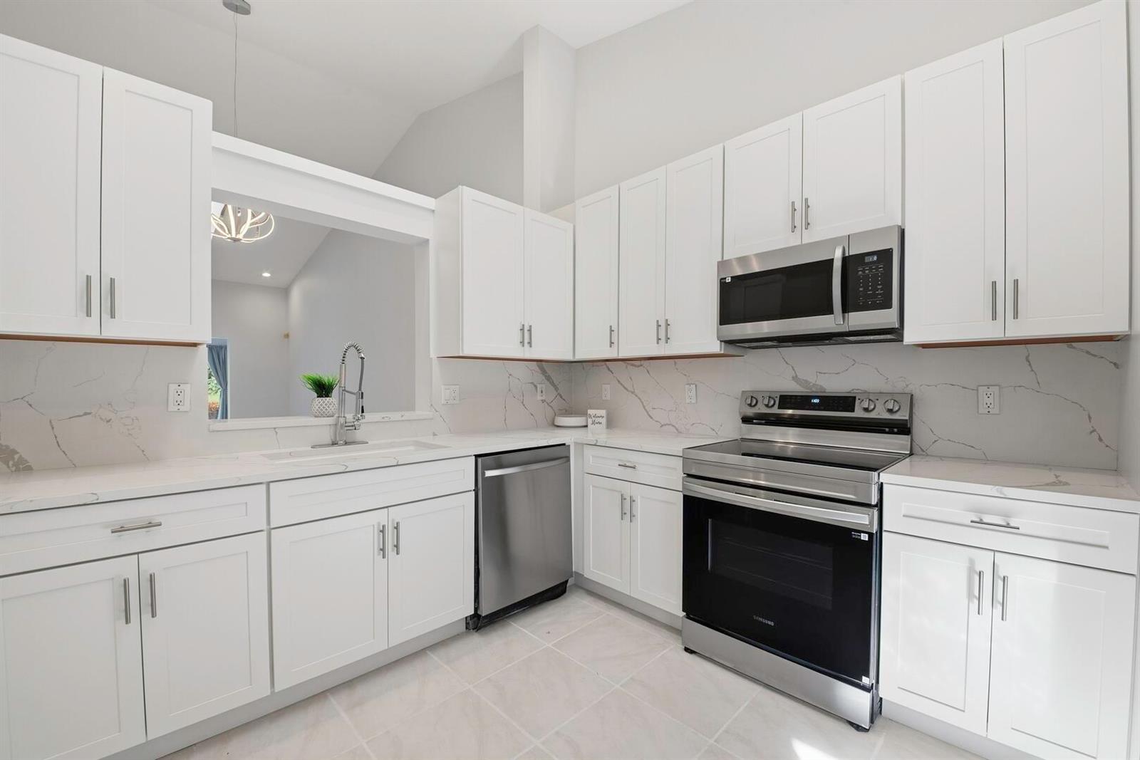 A white kitchen featuring stainless steel appliances, marble-style countertops, and a pass-through window — 7617 Island Breeze Terrace, Boynton Beach FL 33437, BOYNTON BEACH, FL