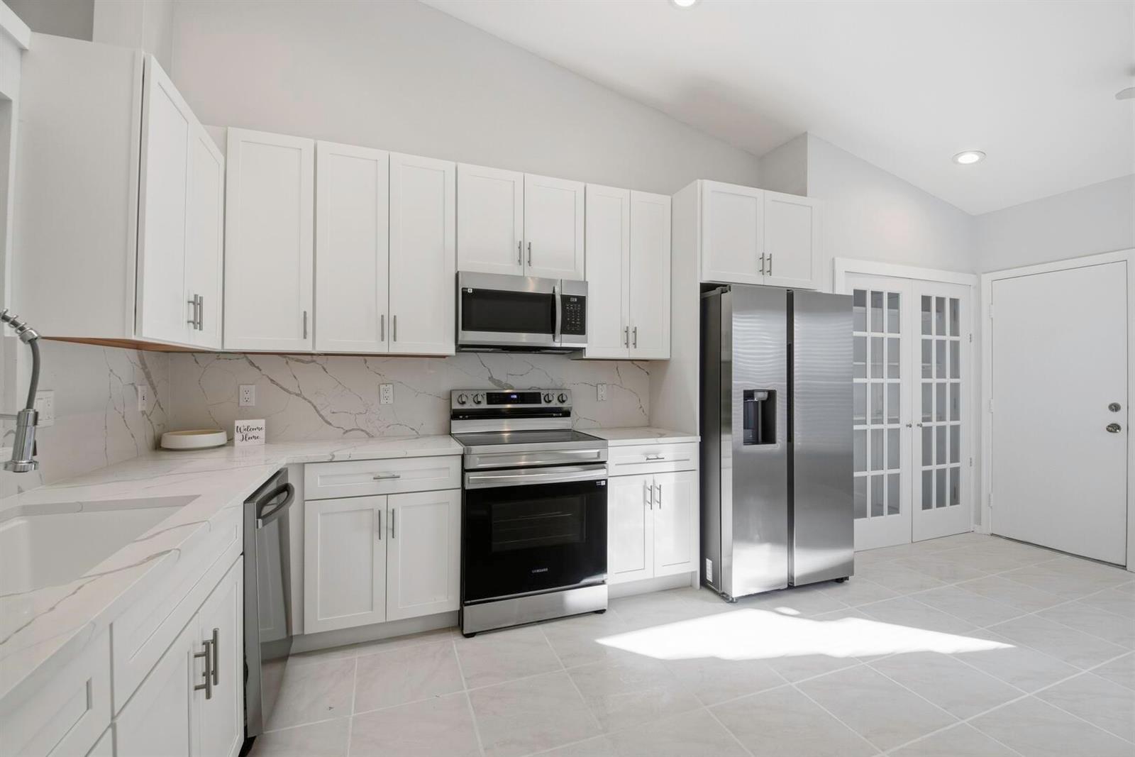A kitchen features white cabinets, stainless steel appliances, and marble-patterned countertops and backsplash — 7617 Island Breeze Terrace, Boynton Beach FL 33437, BOYNTON BEACH, FL