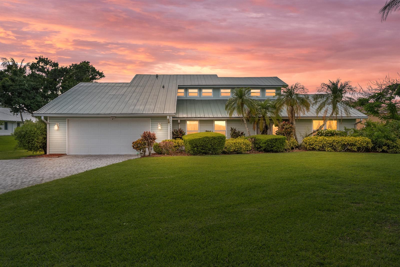 A two-story house with a metal roof and a paved driveway at sunset — 2415 NW Cove View, Stuart FL 34994, STUART, FL