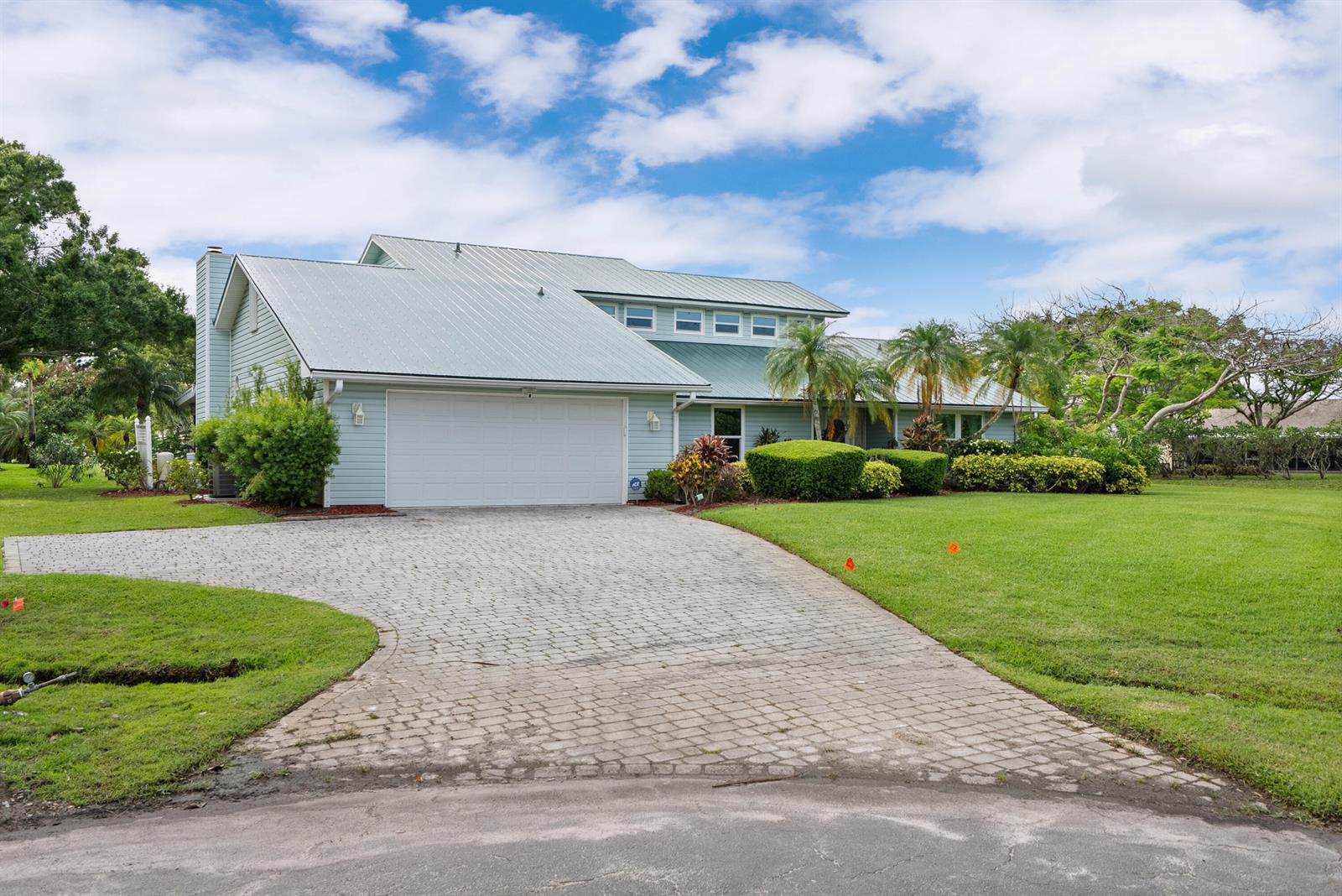 A light blue house with a metal roof and a paved driveway sits on a lawn — 2415 NW Cove View, Stuart FL 34994, STUART, FL