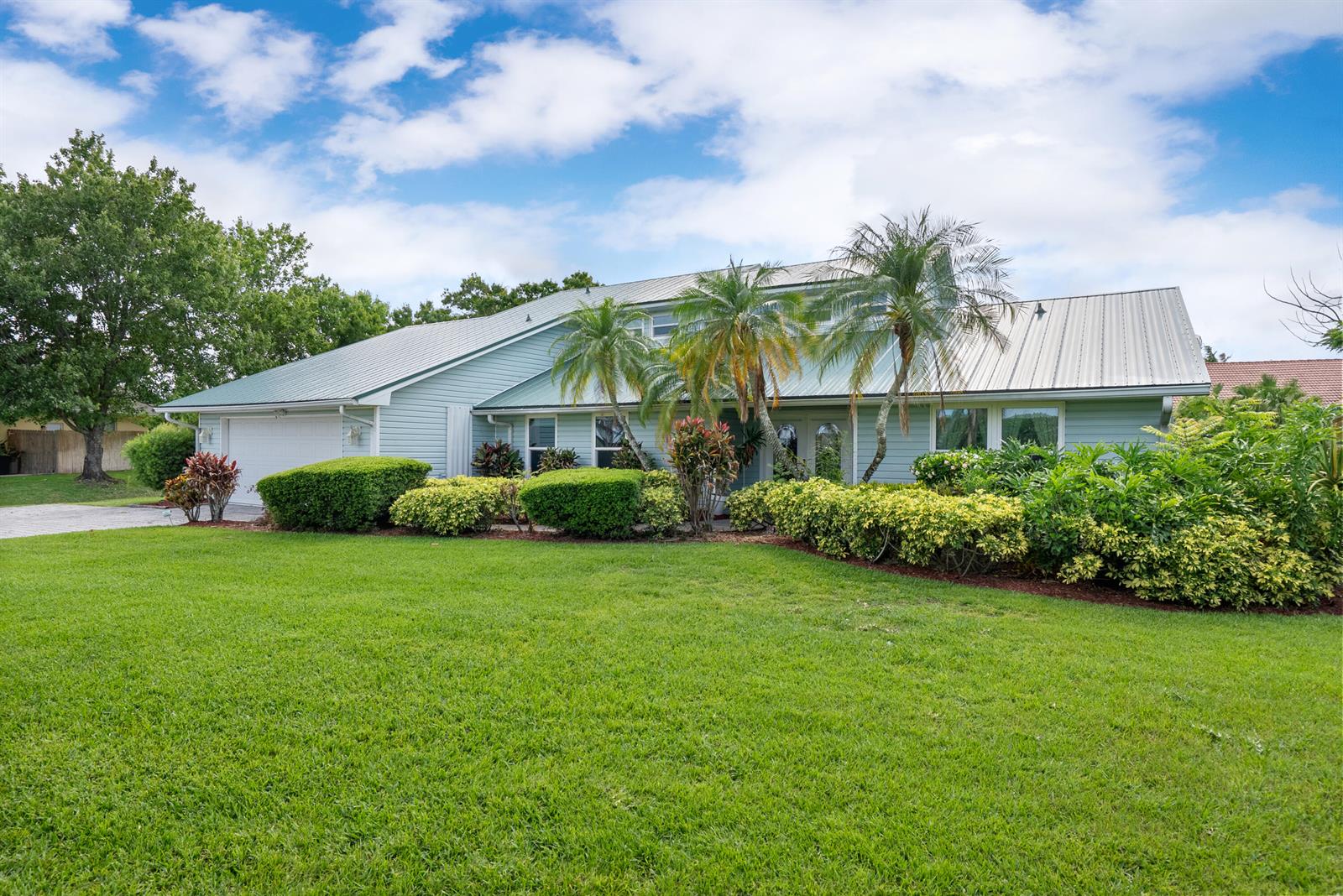 A light blue house with a metal roof and palm trees sits behind a lawn — 2415 NW Cove View, Stuart FL 34994, STUART, FL