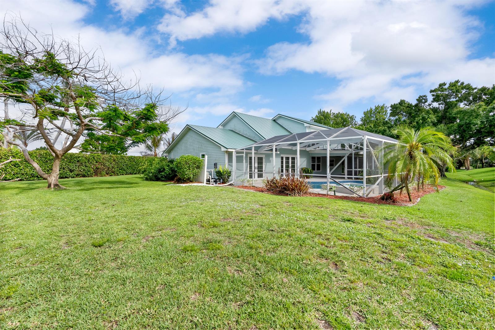 A light blue house with a green metal roof and a screened-in pool area — 2415 NW Cove View, Stuart FL 34994, STUART, FL