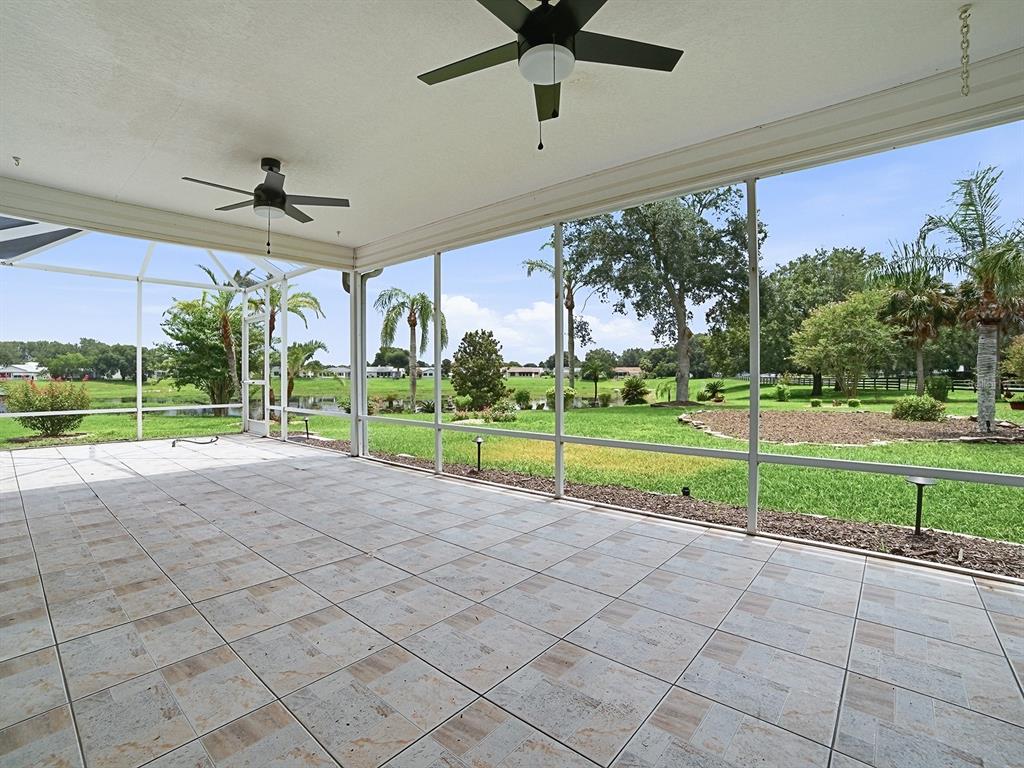 A tiled, screened-in patio overlooks a grassy backyard with trees and a pond — 1611 ALHAMBRA WAY, THE VILLAGES, FL
