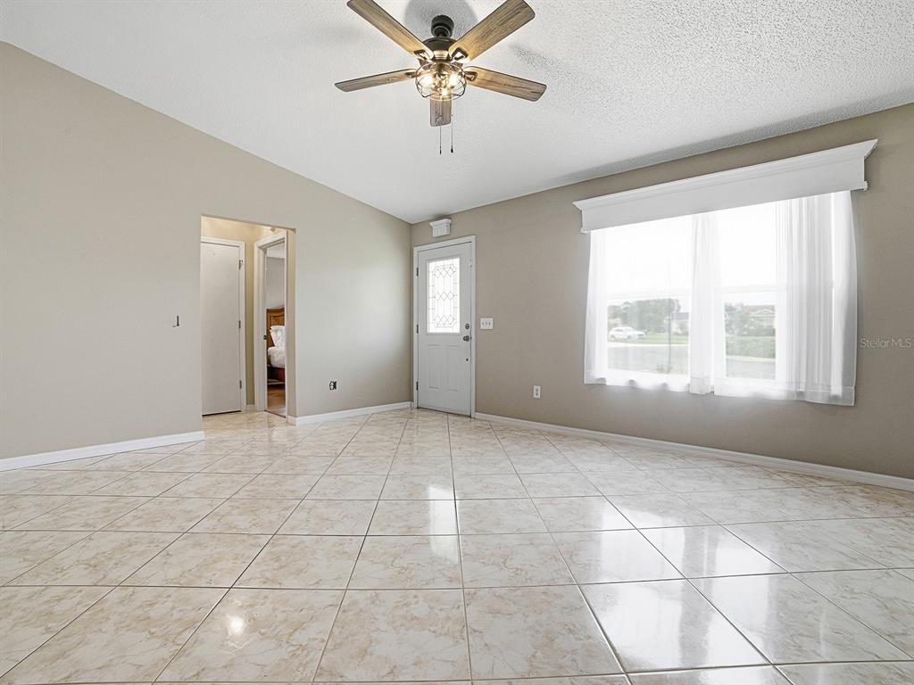 A living room with beige walls, tile flooring, a ceiling fan, and a front door — 1611 ALHAMBRA WAY, THE VILLAGES, FL