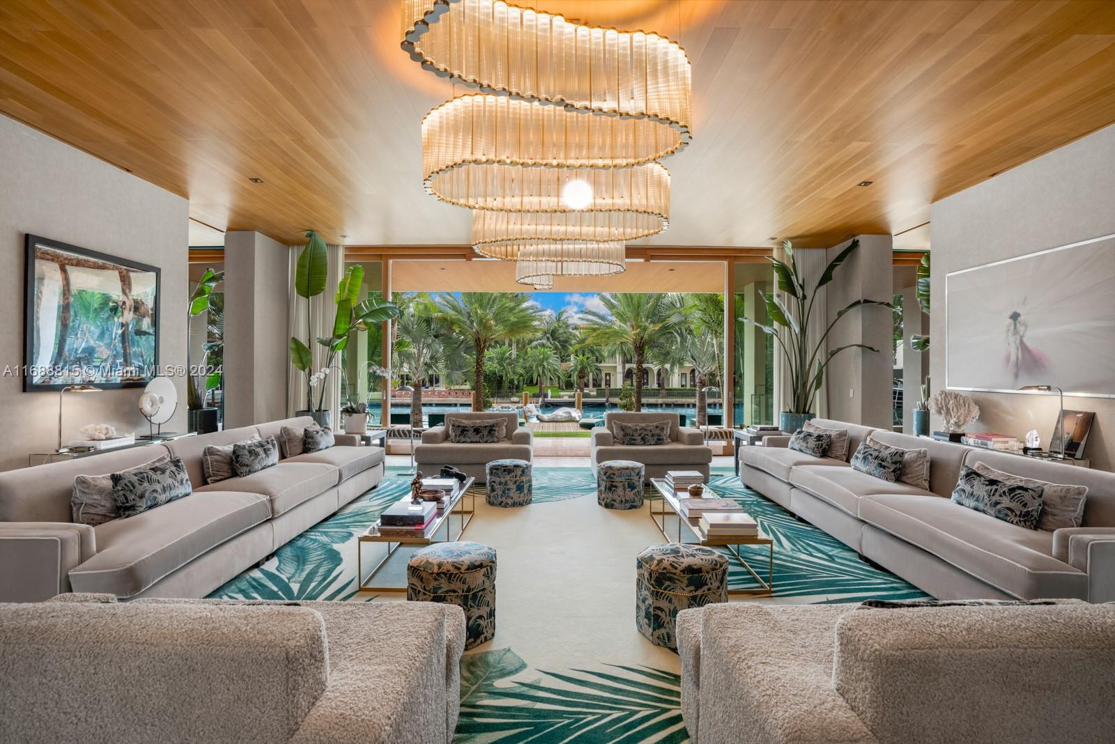 A spacious living room features a large tiered chandelier, neutral sofas, and views of a canal — 1510 W 25th St, Miami Beach FL 33140, MIAMI BEACH, FL
