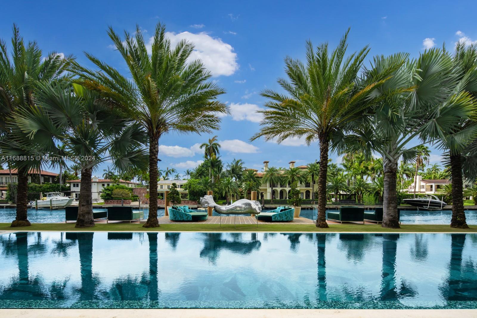 A swimming pool overlooks a canal with palm trees, outdoor seating, and a metal sculpture — 1510 W 25th St, Miami Beach FL 33140, MIAMI BEACH, FL