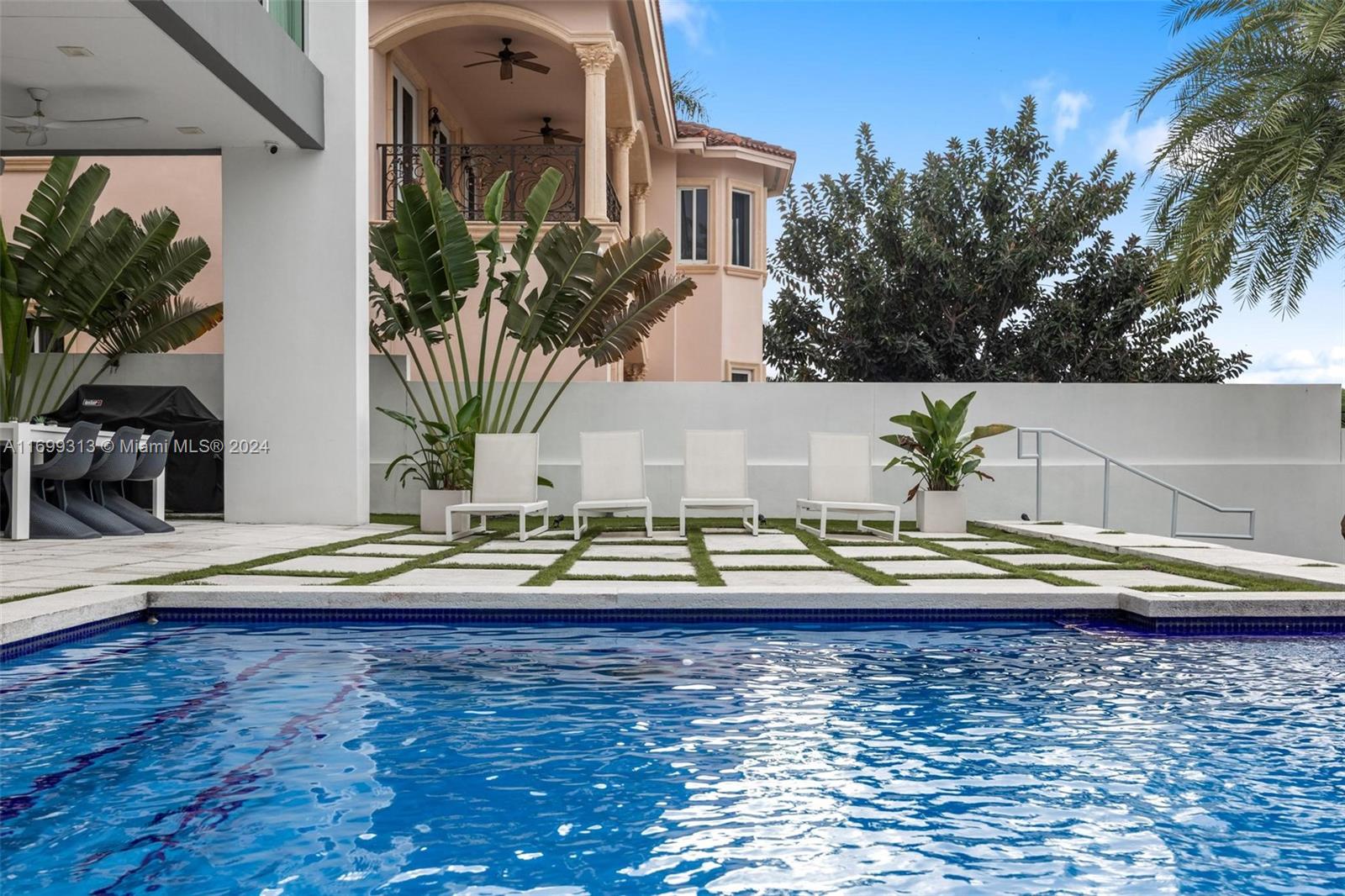 A swimming pool sits in front of a patio with four lounge chairs and plants — 323 Atlantic Ave, Sunny Isles Beach FL 33160, SUNNY ISLES BEACH, FL